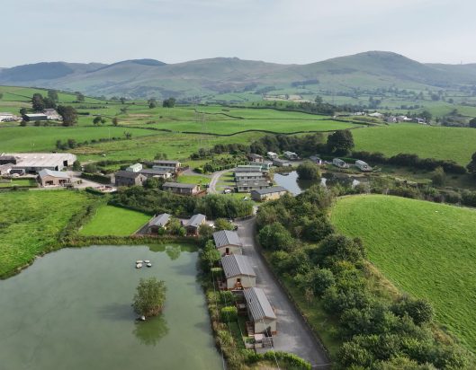 Commercial aerial drone video and photography view of Littlemere Lake District Lodges from the air looking at stunning holiday lets and tranquil pond